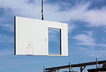 A prefabricated wall with a door cutout hangs mid-air against a cloudy, blue sky