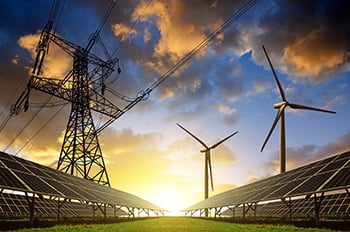 Solar panels with wind turbines and electricity pylon at sunset.