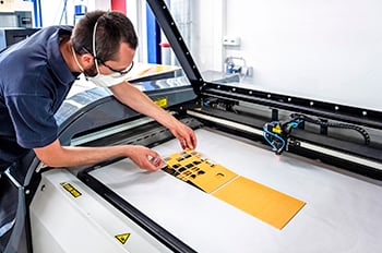 A masked employee carefully positions a die-cut yellow template of material