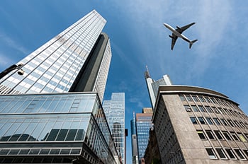 Skyscraper buildings and a plane flying overhead.