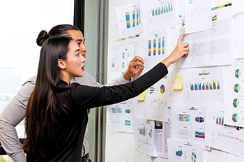A man and a woman in black clothing checking key figures attached to a whiteboard