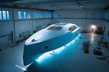 Futuristic boat or yacht made with composite molding technology under construction, suspended in a large hangar.