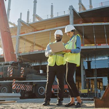 Two people looking at a laptop on a construction site