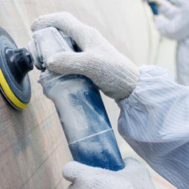 A pair of gloved hands polishes a wind turbine blade inside an industrial setting.