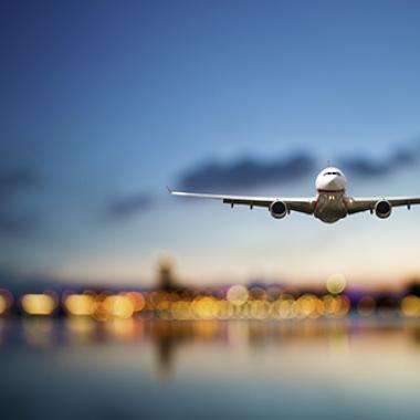 Perspective view of jet airliner in flight with blurred city lights in the background.