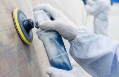 A pair of gloved hands polishes a wind turbine blade inside an industrial setting.