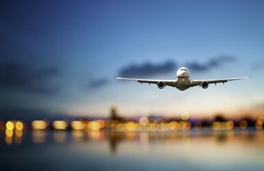 Perspective view of jet airliner in flight with blurred city lights in the background.
