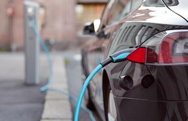 Black electric vehicle charging at charging station.