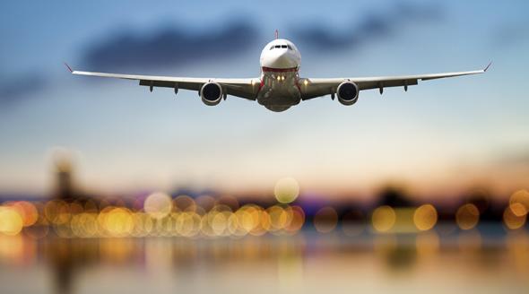 Perspective view of jet airliner in flight with blurred city lights in the background.