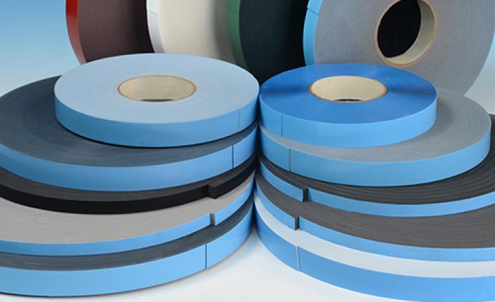 Various bonding tape rolls with different color liners and backings lying and standing in front of a blue gradient.