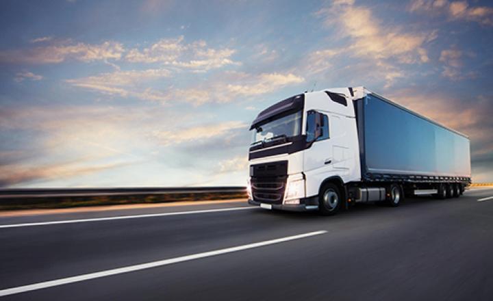 A white tractor trailer truck driving on a highway against a blue, cloudy sky.