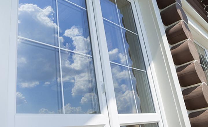 Plastic white glass panels and muntin bars on a log cabin, reflecting a blue sky and clouds.