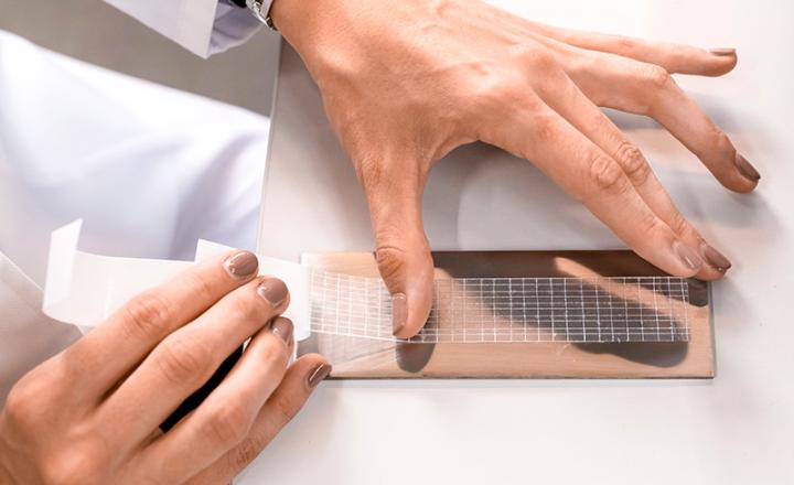 A pair of hands unpeels and applies a clear adhesive tape