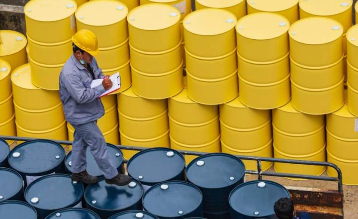 An inspector checking rows of yellow and blue oil drums and stock barrels