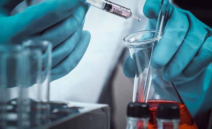 Conical flask in scientist hand with lab glassware.