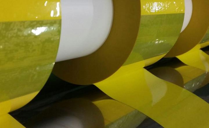Several rolls of yellow tape wound on rod in manufacturing facility.