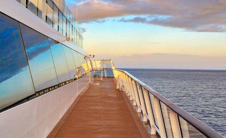 View over the ocean from a cruise ship with glass window front, wooden gangway and ship’s rail.