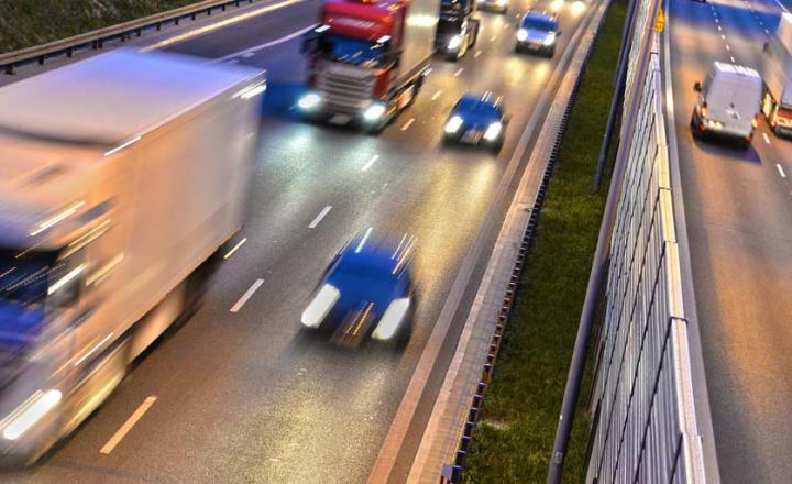 Cars and trucks driving in both directions on a highway with their lights on.