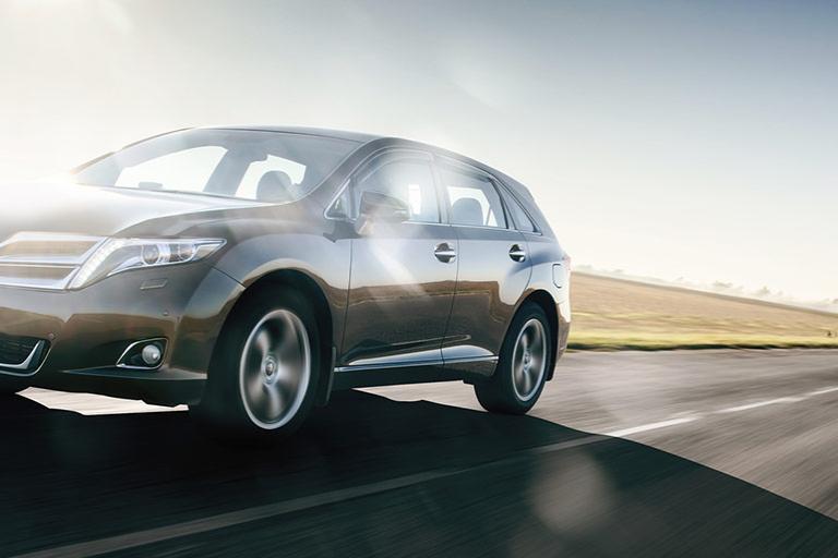 A grey car driving on the open road against a blue sky and sunshine.
