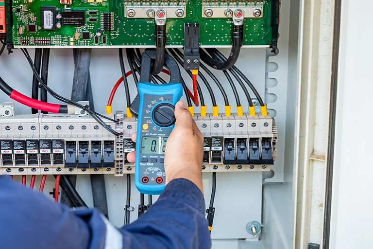 An engineer uses a multimeter to check the operation of a system on a solar farm and panel.