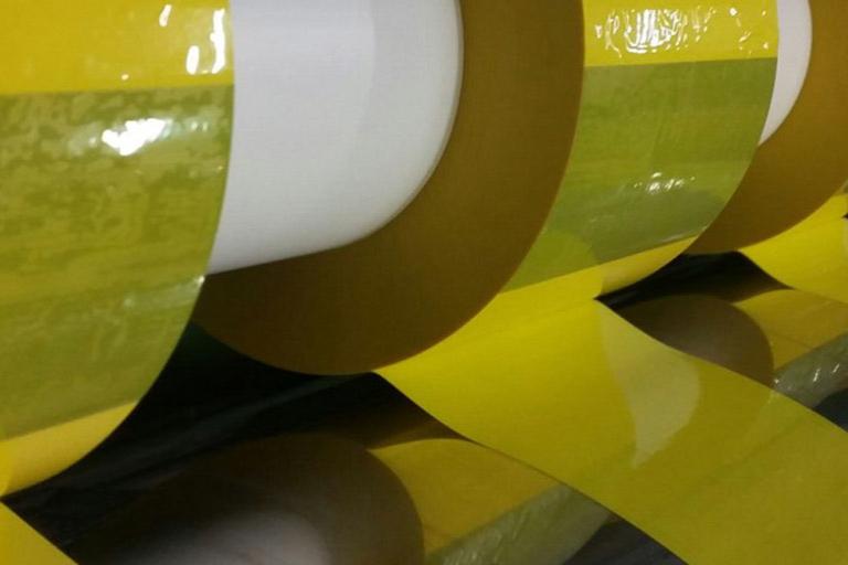 Several rolls of yellow tape wound on rod in manufacturing facility.