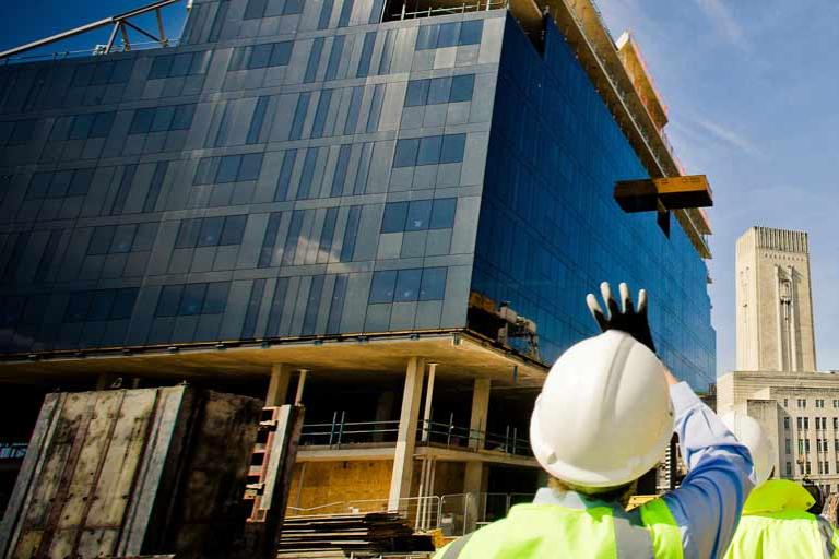 Workers coordinating the construction of a modern office building with glass facades and cladding