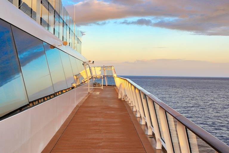 View over the ocean from a cruise ship with glass window front, wooden gangway and ship’s rail.