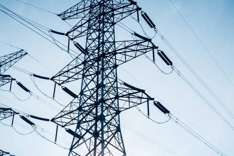 Rows of electric transmission pylons against blue sky.
