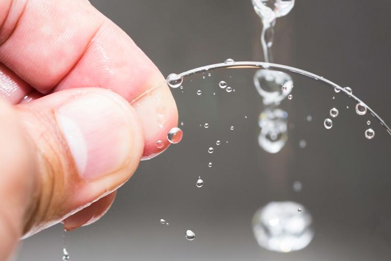 Hand holding a transparent, circular glass lens with clean water droplets streaming down its surface.