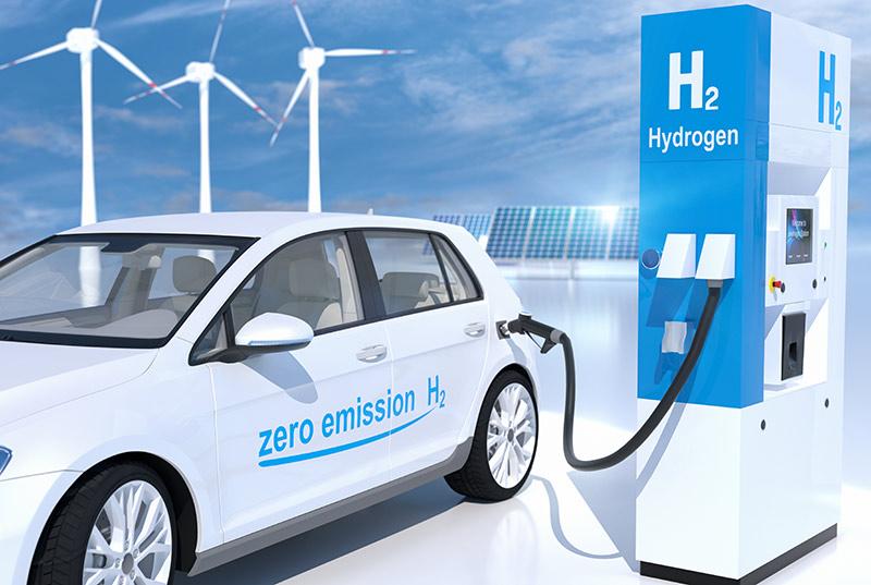 A white car connected to a hydrogen station with renewable energy production in the background