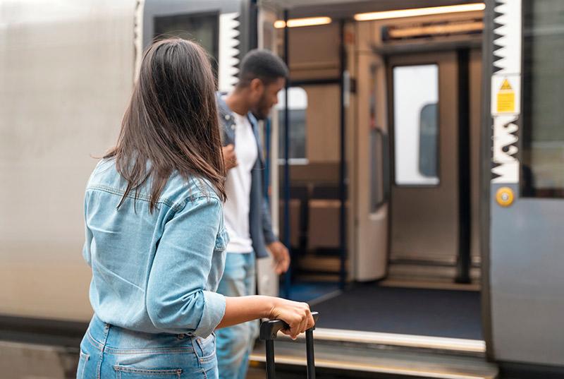 A couple boarding a train with luggage, carpet in the entrance area