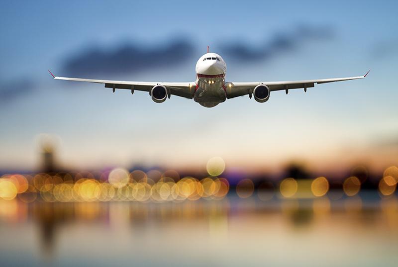 Perspective view of jet airliner in flight with blurred city lights in the background.